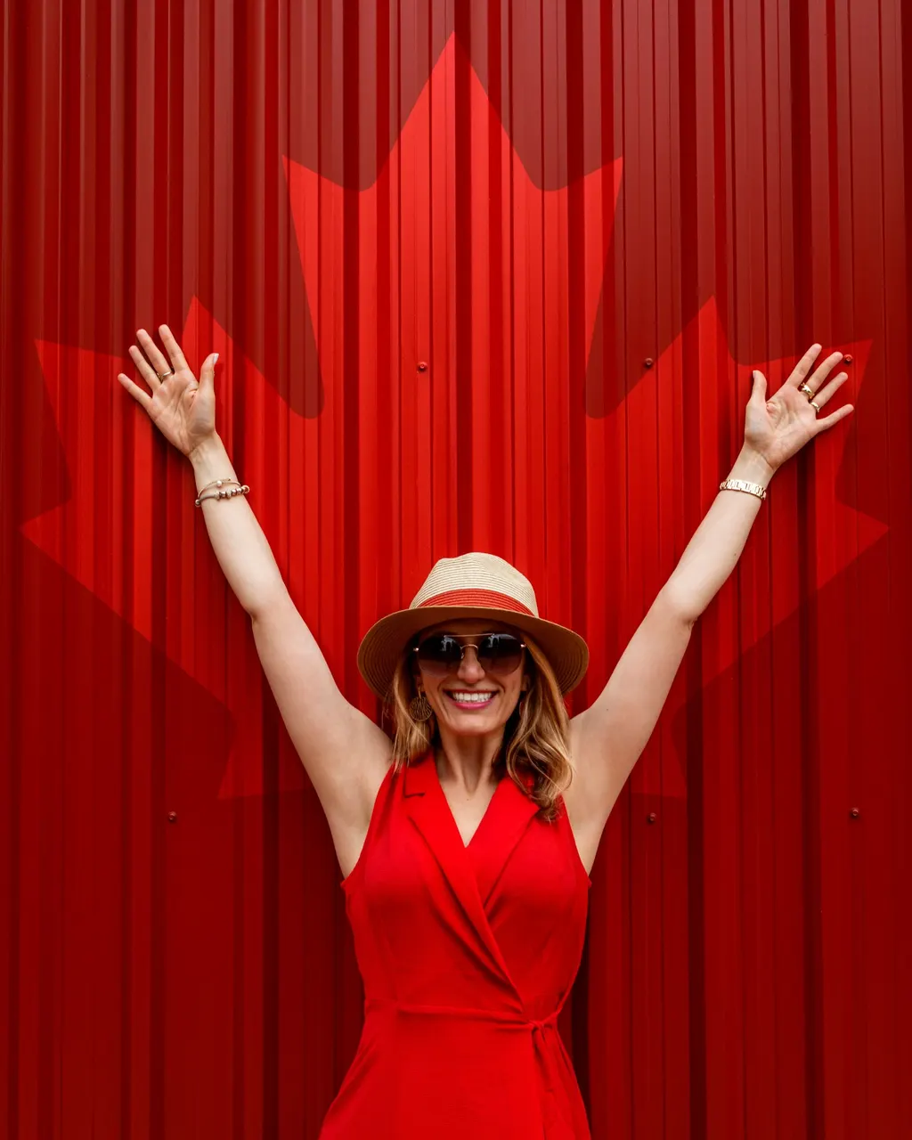 Una viajera con los brazos en alto delante de una pared roja con la hoja de arce de Canadá